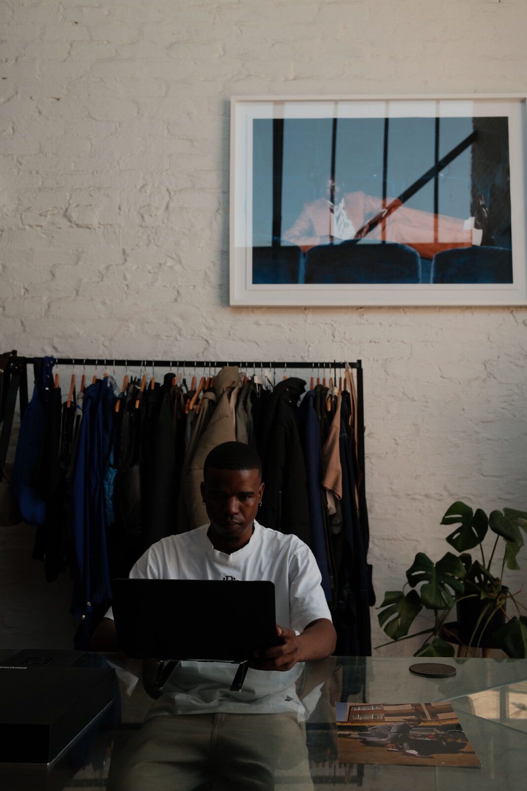 Dineo at the desk with his laptop, garment rack behind