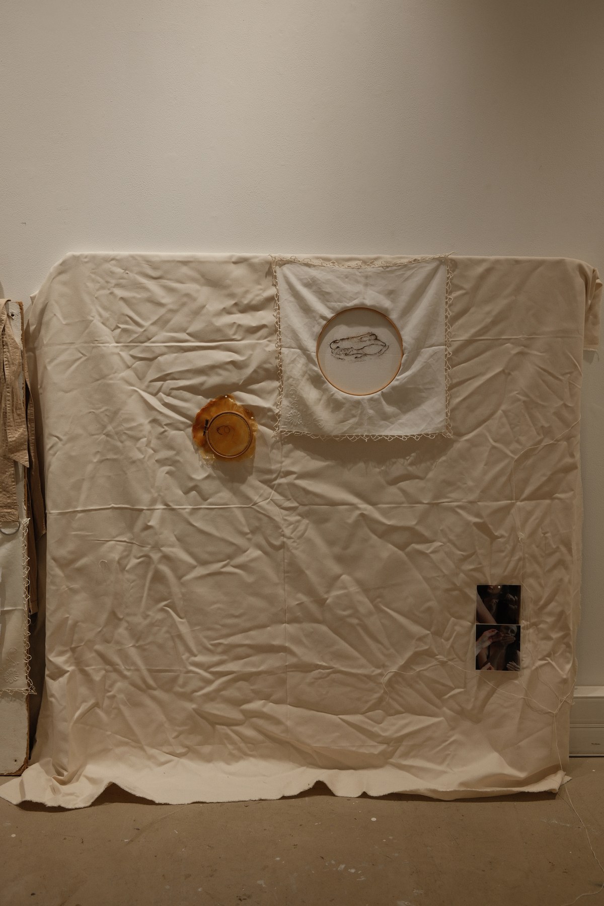 A wider view of the fabric installation — embroidery hoops and small photo prints arranged on a draped cream cloth