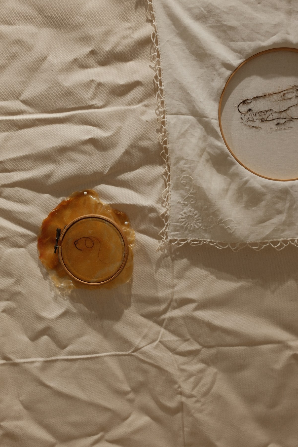 Detail view of the cloth piece showing two embroidery hoops and the delicate lace-edged framing fabric