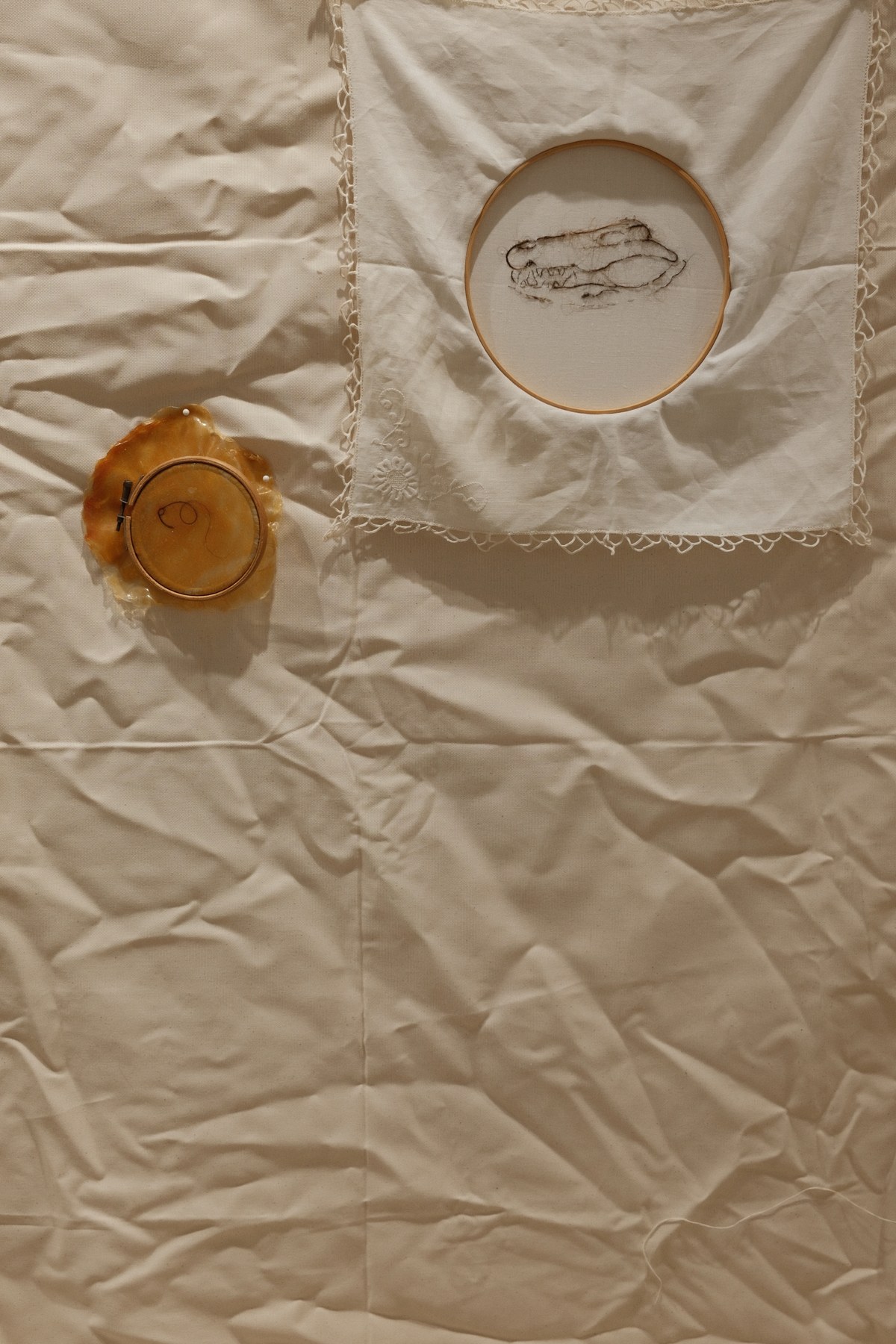 Close-up of two embroidery hoops on cream fabric — one with a curved hair line, the other with a stitched skull form