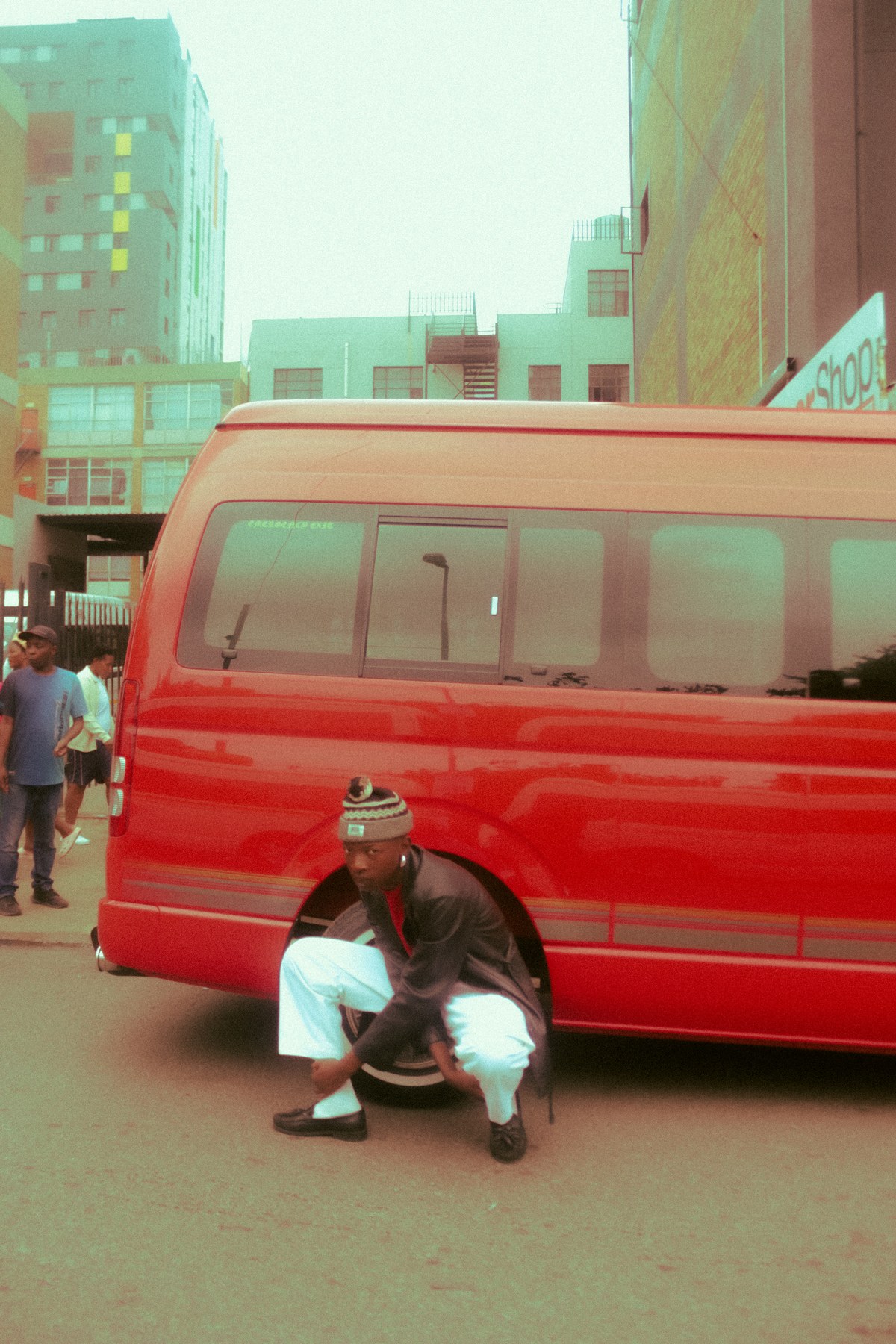 Photograph by Kabelo Matsile — figure crouching beside a red minibus taxi on a Johannesburg street