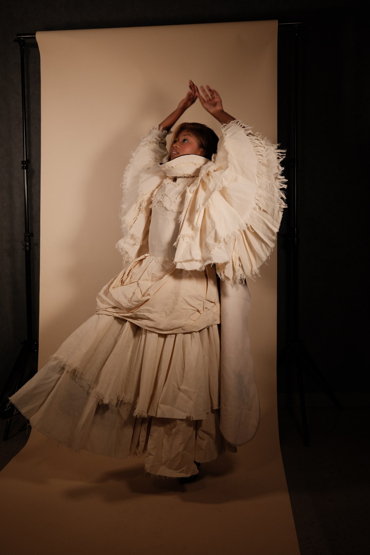 Designed by Mihlali Madikane — a cream tiered gown with a large raw-edged ruffled collar, model arms raised