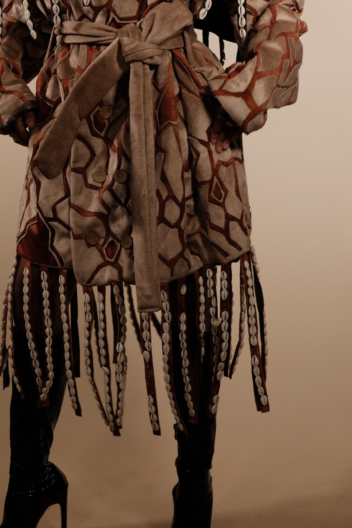 Designed by Mihlali Madikane — geometric velvet and rust patchwork jacket with a wide belt and cowrie shell fringed hem